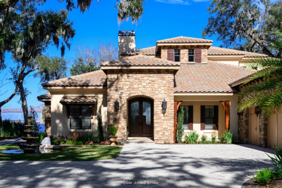 Luxurious Mediterranean-style home with stone accents, tiled roof, and lush landscaping, showcasing elegant architecture and a paved driveway.