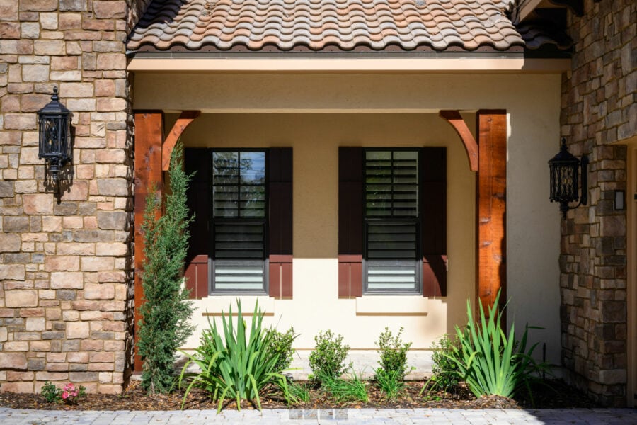 Elegant front porch of a modern home featuring stone and stucco exterior, wooden accents, black shutters, outdoor lanterns, and well-maintained landscaping.