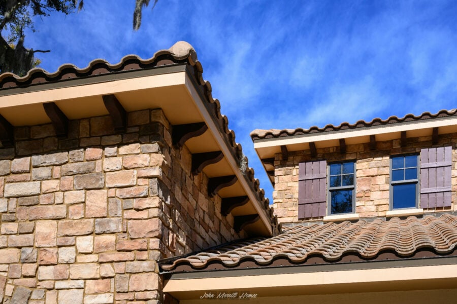Handcrafted stone and stucco exterior of a luxury home with terracotta roof tiles, sky and clouds in the background.