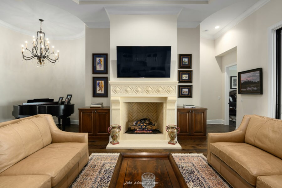 Luxurious living room with a cozy fireplace, a mounted flat-screen TV, elegant artwork, and comfortable beige sofas, showcasing classic interior design and sophisticated decor.