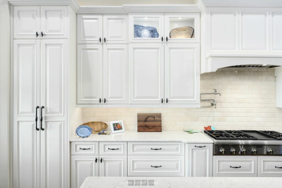 White kitchen cabinetry with black hardware, a beige backsplash, and a modern stainless steel stove, creating a bright and inviting cooking space.