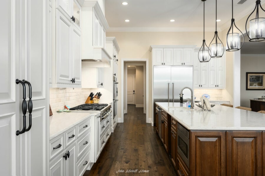 White kitchen with dark hardwood flooring, white cabinetry, stainless steel appliances, marble island, pendant lighting, and beige walls.
