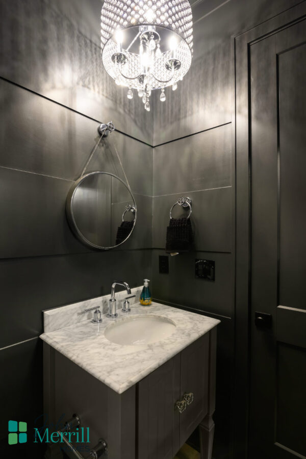 Luxurious black bathroom featuring a marble countertop, round mirror, and ornate chandelier lighting for a sophisticated ambiance.