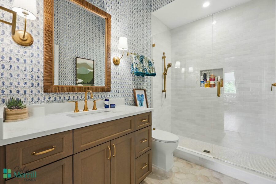 Bathroom with walk-in shower, gold fixtures, and patterned wallpaper.