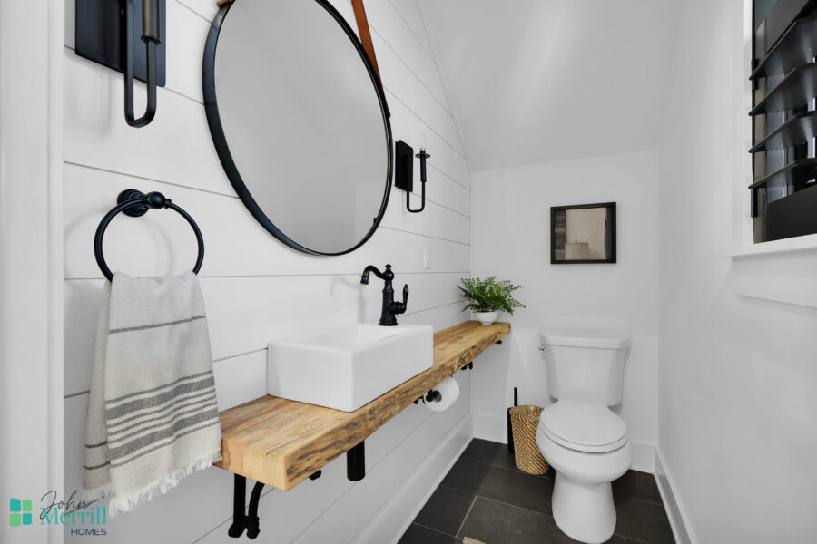 Bathroom with white shiplap walls, black fixtures, a wooden vanity with a vessel sink, and a toilet, creating a clean and stylish space.