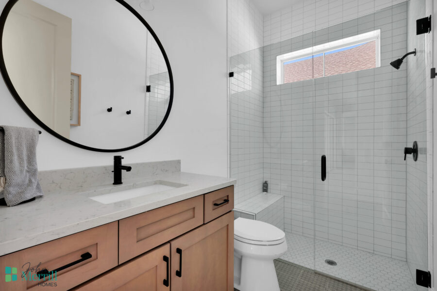 Bright bathroom featuring a large mirror, white tiled walls, and a walk-in shower with black fixtures.