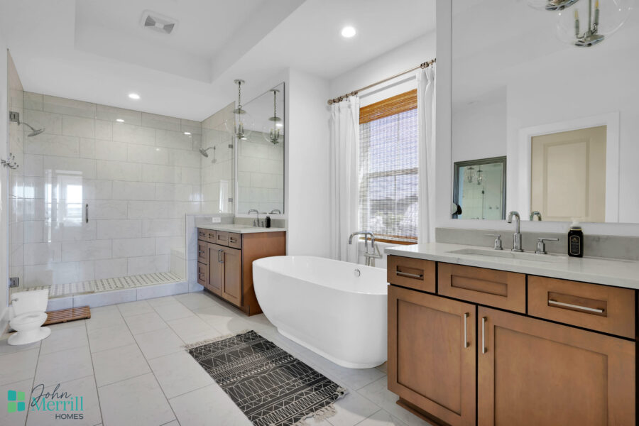 Spacious bathroom featuring a sleek freestanding bathtub, a large walk-in shower with glass doors, and elegant wooden cabinetry under a bright window.