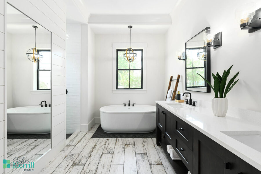 Bright and spacious bathroom featuring a sleek freestanding bathtub, large windows providing natural light, and a stylish double vanity with black cabinets and white countertop.