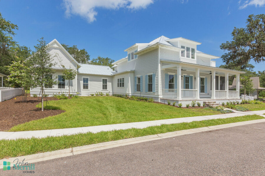 A white, two-story house with a wraparound porch, large windows, and a well-maintained lawn, showcasing a contemporary residential design by John Merrill Homes.