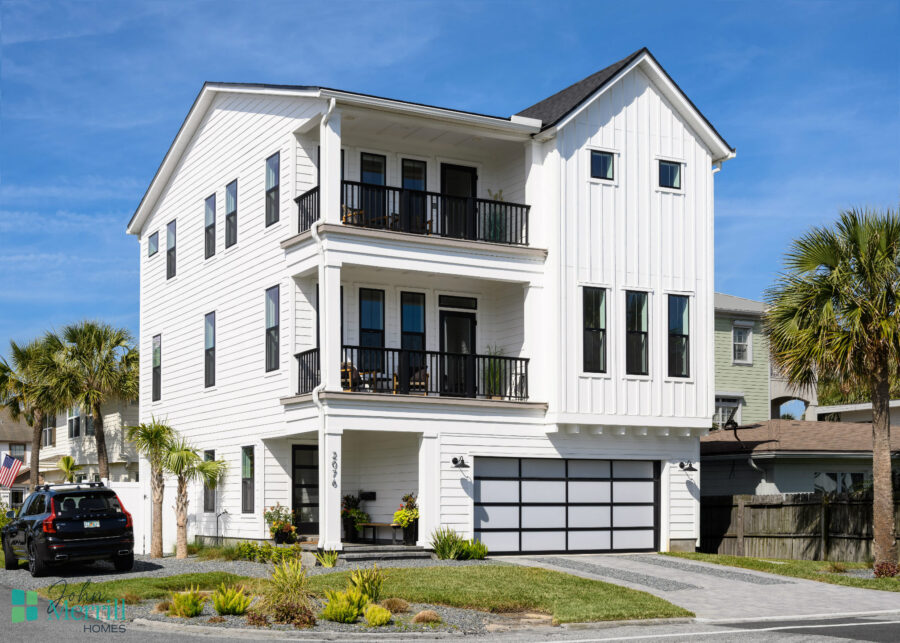 A spacious white coastal-style home featuring multiple balconies, large windows, and a two-car garage, set against a bright blue sky with palm trees in the background.
