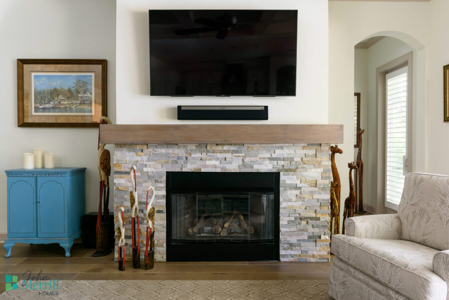 A modern living room featuring a stone fireplace with a mounted flat-screen TV above, complemented by a blue side table and comfortable beige sofa.