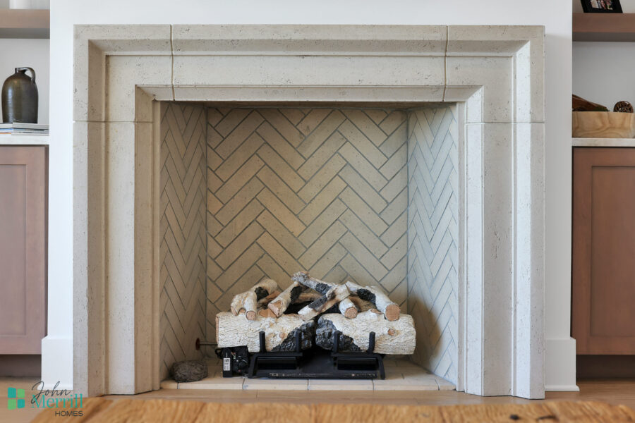 A modern fireplace featuring a clean, beige stone surround and a neatly arranged stack of decorative logs inside. The fireplace adds warmth and style to the living space.