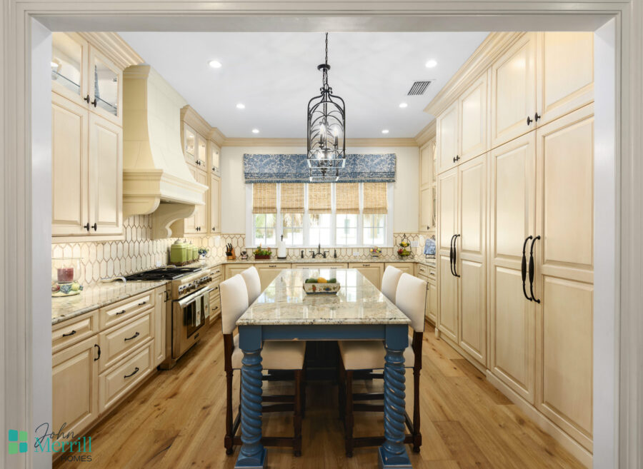 Bright and inviting kitchen featuring cream-colored cabinetry, a central island with blue legs, and a large window with a blue valance providing natural light.