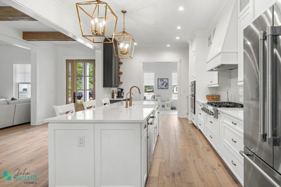 A bright, modern kitchen featuring white cabinetry, a large island with a sink, stainless steel refrigerator, and elegant pendant lighting, perfect for contemporary home living.