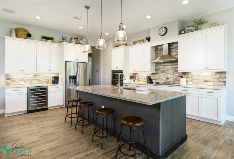 Spacious kitchen featuring white cabinetry, a large island with seating, stainless steel refrigerator, oven, and range hood, illuminated by pendant lights.