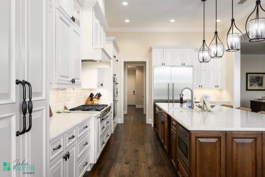 Bright and spacious kitchen featuring white cabinetry, a large dark wood island, stainless steel appliances, and pendant lighting, perfect for family cooking and entertaining.