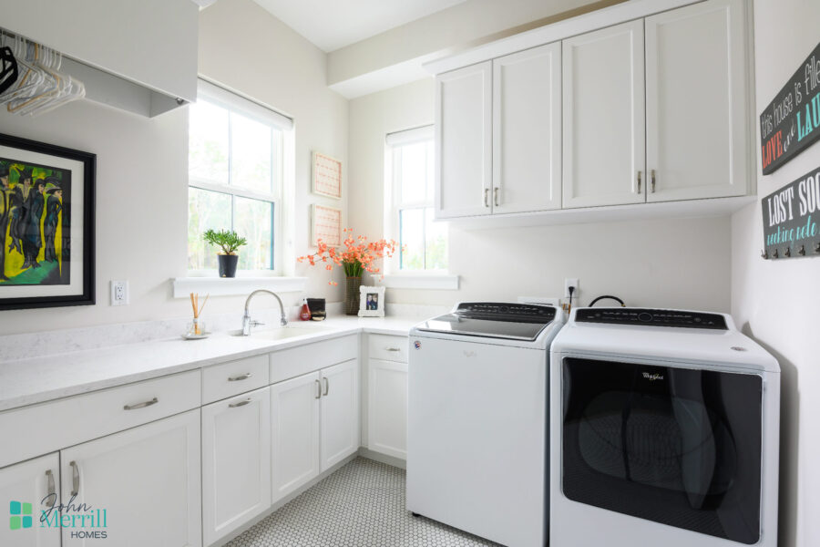 A bright laundry room featuring white cabinetry, a washer and dryer, and natural light from two windows, creating a clean and functional space.