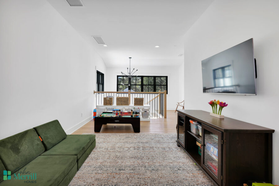 Bright and spacious living room featuring white walls, large windows, and contemporary furniture, including a green sofa, a TV mounted on the wall, and a wooden entertainment unit.