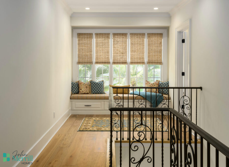 Bright interior with a cozy window seat featuring cushions and bamboo shades, overlooking a lush outdoor view.