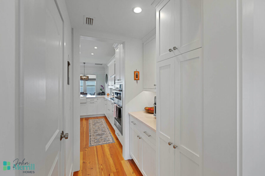 Bright and modern white kitchen with wooden flooring, cabinetry, and stainless steel appliances, featuring a cozy and functional space for cooking and dining.