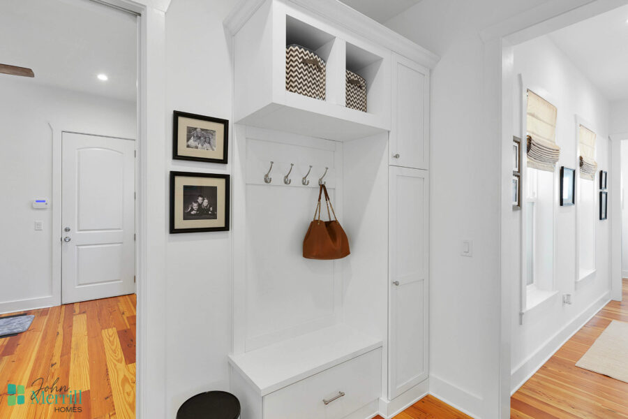 Bright and clean entryway featuring a built-in storage bench, hooks for coats, and decorative wall art, creating an inviting space in a contemporary home.