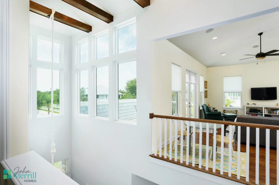 Sunlit living room featuring expansive windows that bring in natural light, high ceilings with wooden beams, and a cozy seating area with a TV and decorative accents.