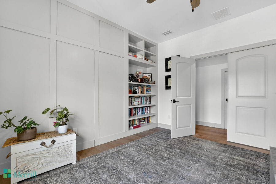 Bright, modern interior room with white walls, built-in bookshelves, and a door, featuring a cozy rug and decorative plants.