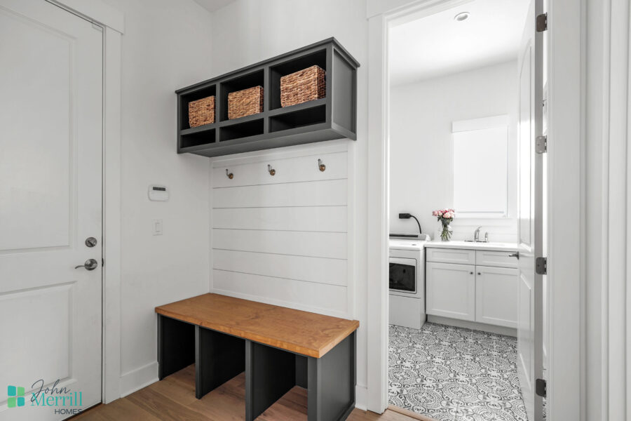 Bright and clean mudroom featuring a wooden storage bench, wall hooks, and overhead cubbies with woven baskets for organization.