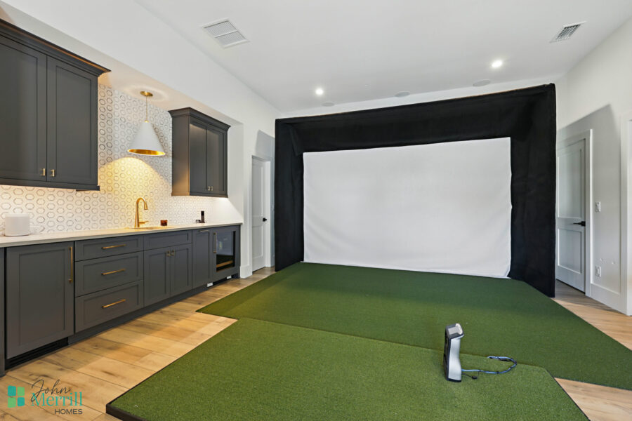 Interior view of a home theater room featuring a large projection screen, green carpet, and modern kitchen cabinets in the background.