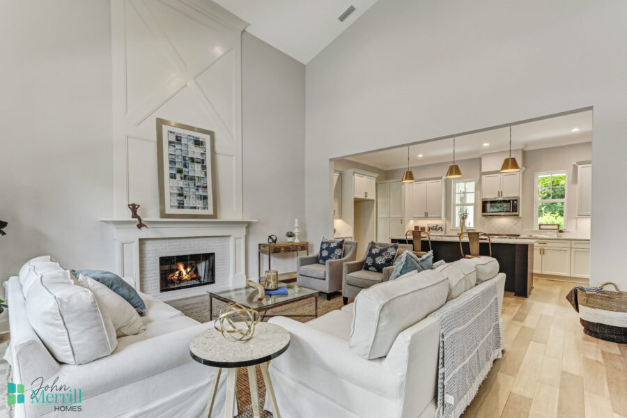 Spacious living room featuring a cozy fireplace, white sofas, and a view into the open kitchen with pendant lighting and large windows for natural light.