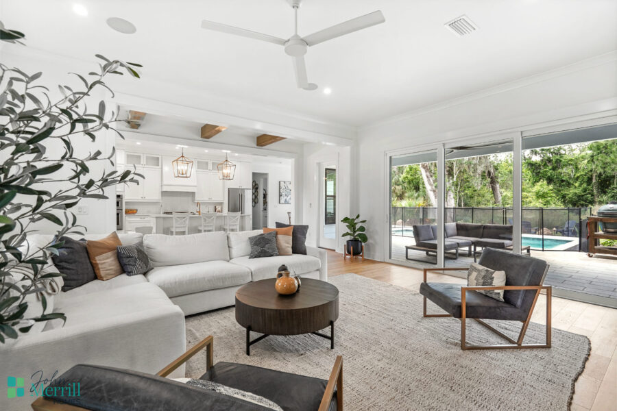 Spacious living room featuring a white sectional sofa, contemporary armchairs, and large sliding glass doors that open to a backyard pool area. Bright, airy, and perfect for relaxing or entertaining.