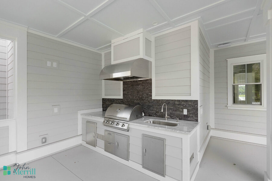 Outdoor kitchen with stainless steel grill, sink, and storage cabinets in a bright, modern setting.
