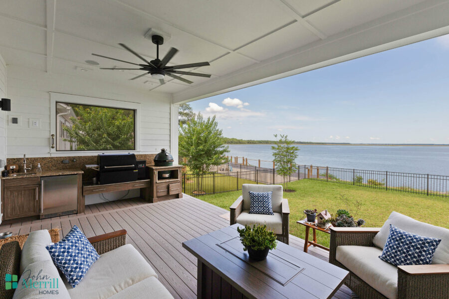 A spacious covered porch overlooking a serene lake with outdoor seating, a ceiling fan, and a view of the water and sky, perfect for relaxing and enjoying nature.