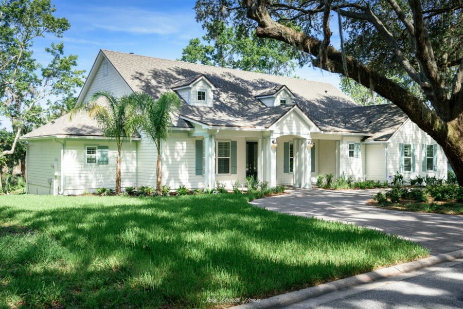 Beautiful white single-family home with a landscaped front yard, tall palm trees, and a large shaded oak tree, showcasing elegant architecture and lush greenery.