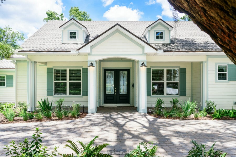 Luxurious modern home with white siding, green shutters, and a paved walkway, showcasing a charming front door and landscaping, ideal for homebuyers seeking elegant, functional living spaces.