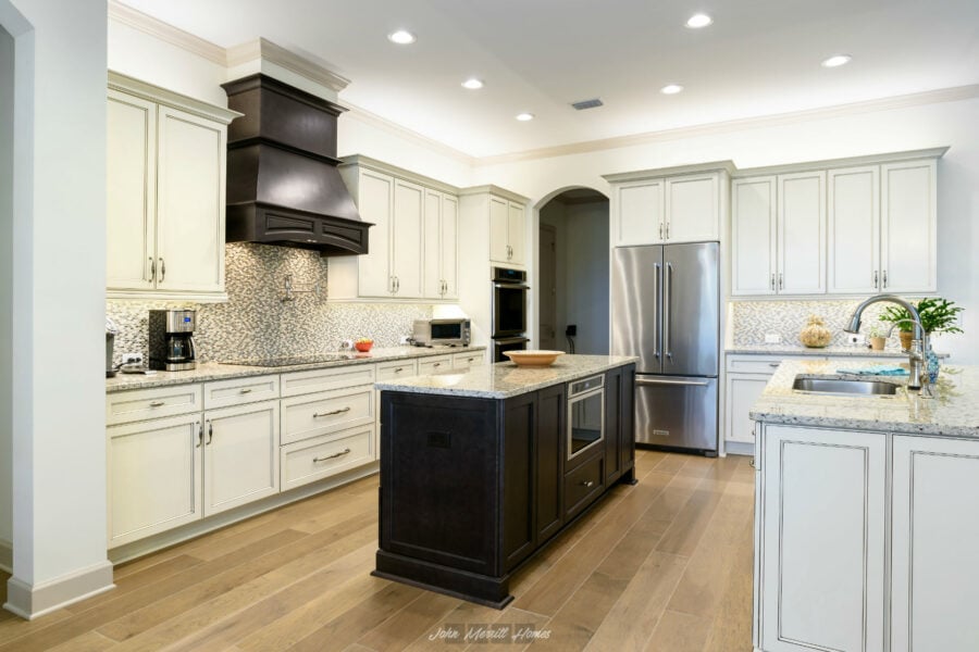 Modern kitchen with white cabinets, granite countertops, stainless steel appliances, and a central black island for cooking and prep. Elegant mosaic backsplash and recessed lighting enhance the space.