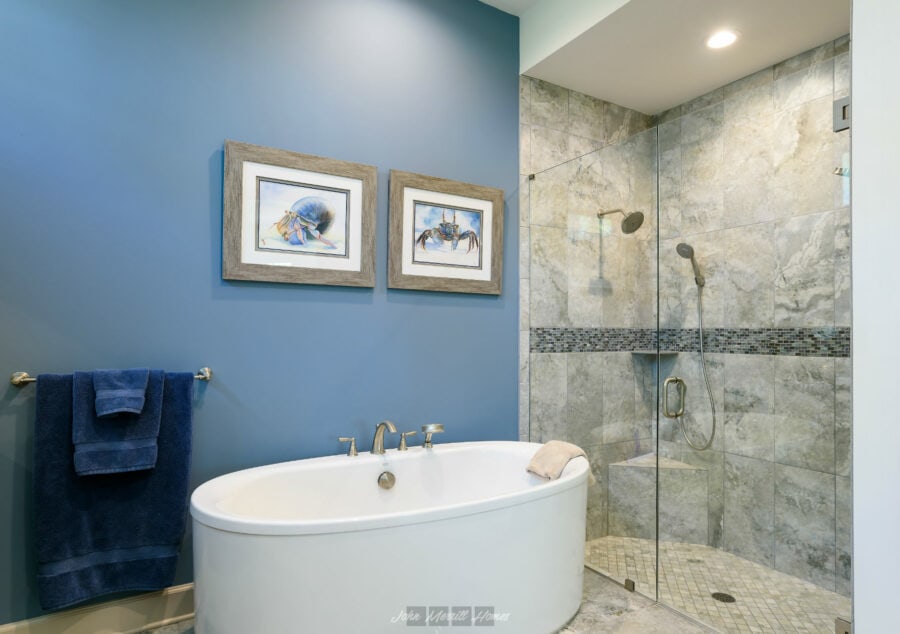 Stylish bathroom featuring a modern freestanding bathtub and a spacious glass-enclosed shower with marble tiles and a decorative mosaic band. The blue accent wall adds a relaxing, contemporary touch.