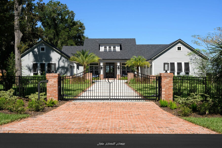 Gated front entrance of a modern home with white siding, black accents, and lush landscaping, showcasing expert craftsmanship and elegant curb appeal.