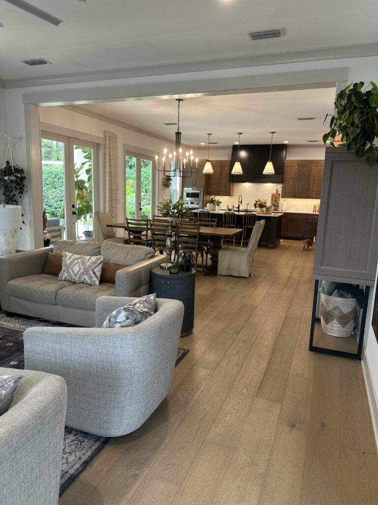 Bright open-concept living and dining area with large windows, neutral-toned furniture, and a modern kitchen featuring dark wood cabinets and pendant lighting. Perfect for family gatherings and entertaining guests.