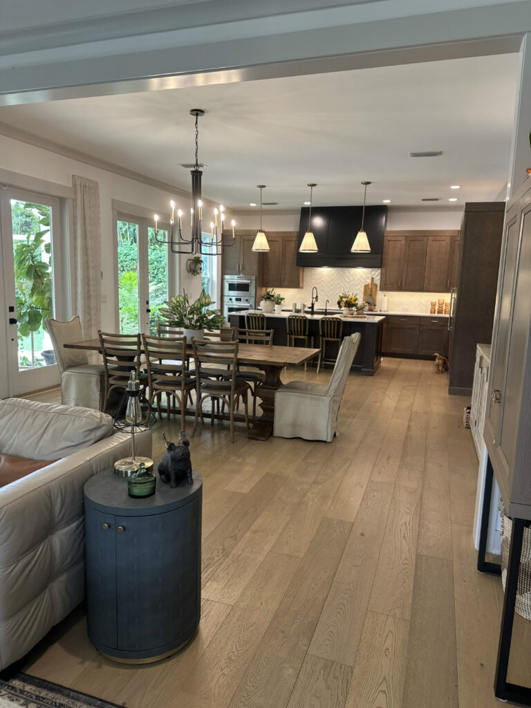 1. Bright open-concept kitchen and dining area with rustic wood flooring, modern appliances, and elegant lighting fixtures in a stylish home by John Merrill Homes.