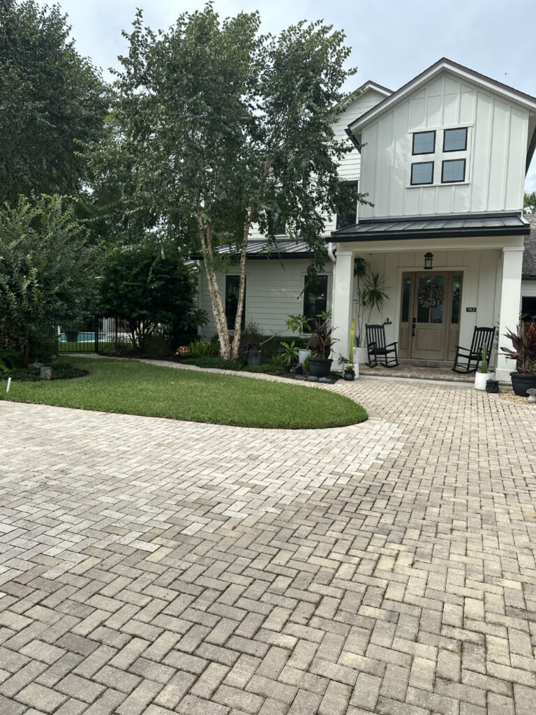 1. Modern white two-story house with front porch, surrounded by lush landscaping and a brick paver driveway, in a sunny setting.