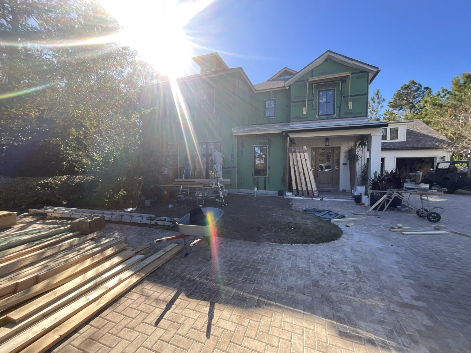 1. New two-story house under construction with green sheathing and partially finished exterior in a sunny residential neighborhood.