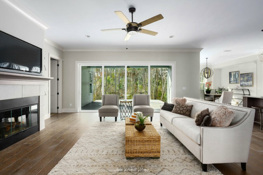 Bright and spacious living room featuring large sliding glass doors overlooking a wooded outdoor area, with modern decor, a cozy fireplace, and comfortable seating.