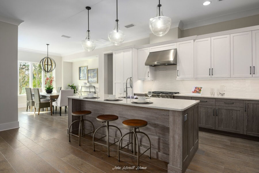 Modern open-concept kitchen with white cabinetry, stainless steel appliances, and a large island with seating, featuring pendant lighting and a view into the adjacent dining and living areas.