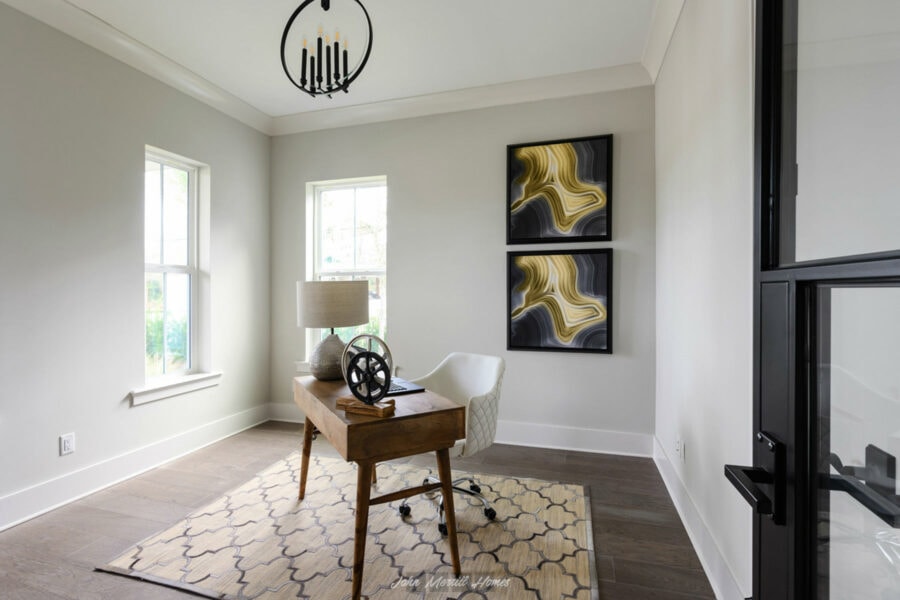 Modern home office with white walls, two windows, a wooden desk, a white swivel chair, and abstract artwork, featuring contemporary decor and natural light.