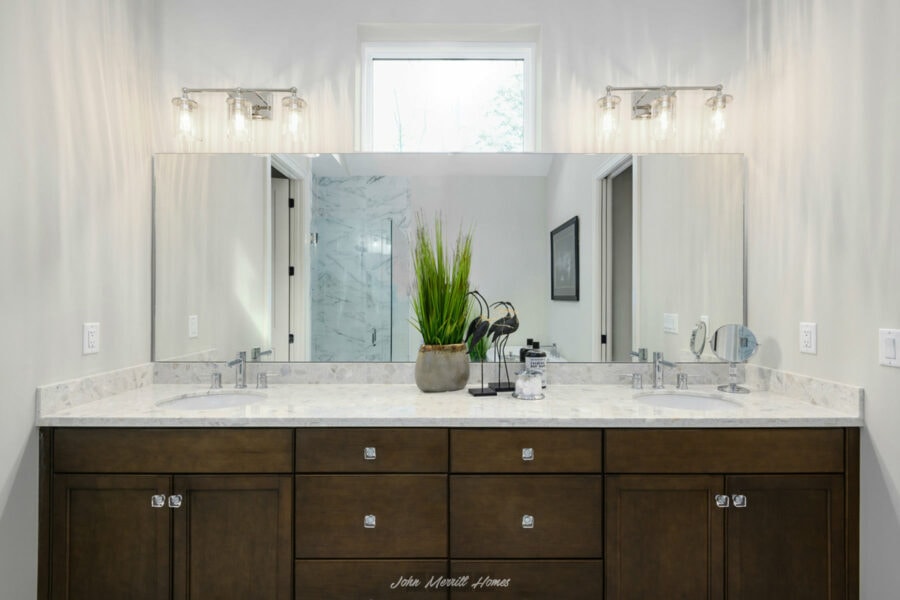 Bright modern bathroom vanity with dual sinks, wooden cabinets, marble countertop, large mirror, and contemporary lighting fixtures, providing a sleek and functional space.