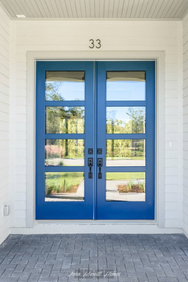 Modern blue front entry door with glass panels, black hardware, and house number 33 above, set against white exterior walls with a brick walkway leading up to the entrance.