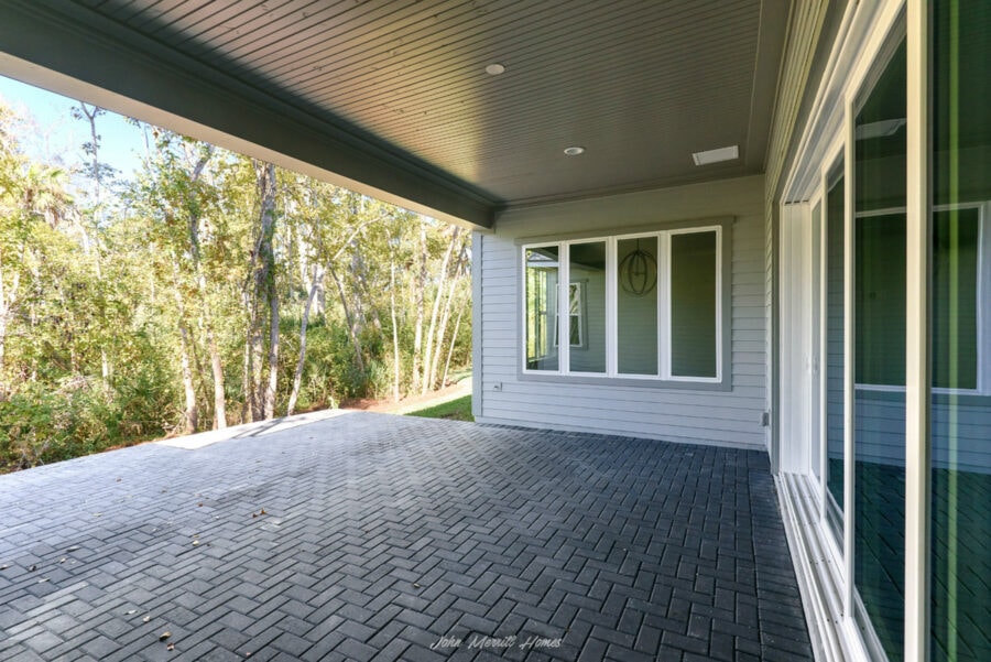 Spacious covered outdoor patio with gray paver flooring and views of lush trees, ideal for relaxing and entertaining in a modern home.