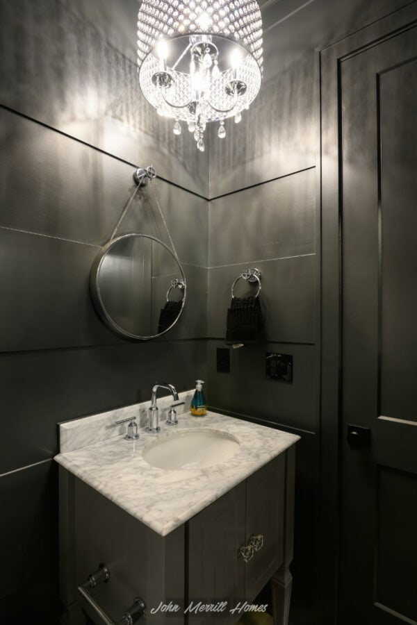 Elegant modern bathroom vanity featuring a marble countertop with an under-mount sink, complemented by sleek chrome fixtures, a decorative round mirror, and a chic chandelier providing ambient lighting.