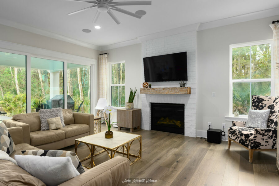 Modern living room with large windows, a white brick fireplace with a mounted TV, and stylish beige and patterned seating; bright, airy space with natural light and contemporary decor.